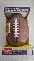 Full view of football in original box labeled 'National Champions' and 'Rawlings Full Size Football Kicking Tee Included'