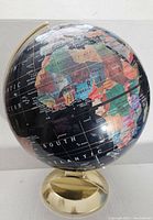 Close-up photo of the globe showing Africa, Europe and part of South America with colorful country borders on a dark background, supported by a gold metal stand.