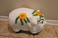Side view of the large pig-shaped chalkware piggy bank showing yellow flower and green leaf decorations on white body.