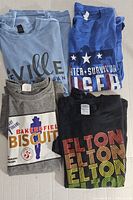 Four assorted music artist and band t-shirts stacked and folded.