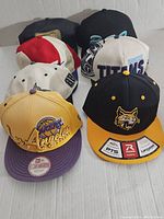 Eight hats arranged in two rows including a yellow Los Angeles Lakers hat and white Tennessee Titans hat, showing front logos.