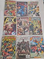Photo showing nine vintage Avengers comic books arranged in a 3x3 grid. Covers include classic Marvel superheroes and vibrant artwork.