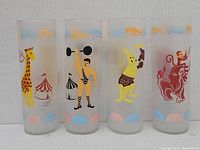 Four vintage Libbey circus glasses in a row showing colorful circus characters and tents.
