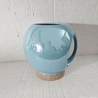 Front and side view of the light blue, round-shaped ceramic mug with tan base labeled 'Life Orb'.