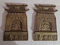 Front view of both brass pagoda bookends showing pagoda roof details, engraved brick pattern, floral designs, and characters at base.
