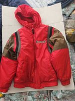 Full front view of the reversible youth coat showing the bright red exterior with hood and elastic cuffs and waistband.