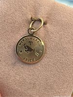 Close-up front view of a small round gold Aries zodiac pendant showing detailed engraving of the Aries ram symbol, symbol, dates 'Mar 21 - Apr 19' and word 'Aries'.