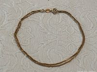 Small delicate gold bracelet laid flat on fabric background.