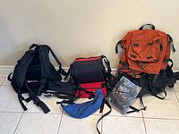 Wide view showing all backpacks and bags arranged on tile floor against beige wall