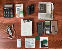 Full lot showing calculators, laser pointers, voice recorder, cables, manuals, and resource disks laid out on wooden surface.