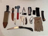 Overview of the complete lot showing all items arranged on a surface including knives, hatchet, saw, multi-tool, carabiner, gloves, and sheath holders.
