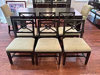 Front view of six dark wood contemporary dining chairs with beige seat cushions arranged in two rows of three in a dining room setting.