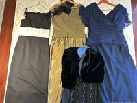 Four evening dresses displayed with hangers, showing full length and details including a black dress with matching bolero jacket.