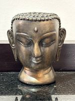 Front view of the metal Buddha head sculpture showing facial features and texture of the metal.