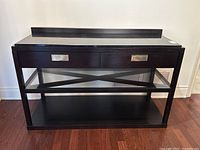 Front view of the Michael Weiss granite top console table showing dark espresso finish, two drawers with metal handles, glass shelf with X-shaped framing, and bottom wooden shelf.