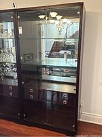 Front view of black Michael Weiss glass display cabinet showing glass doors, shelves, and drawers.
