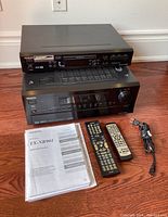 Overall view of Onkyo receiver and DVD player stacked with remotes, power cord, and instruction manuals laid out on floor.