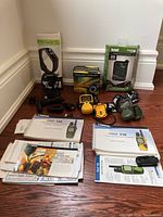 Wide view showing the entire lot including Fitbit Charge 2 with charger, Garmin Rino radios, Bushnell GPS in box, and manuals spread out.