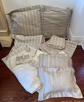 Beige and cream queen sheet set with decorative pillows and curtains arranged on the floor.