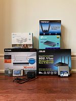 Photo showing boxed Asus RT-AC66U router, D-Link Xtreme N router, TrendNet AC1900 USB adapter, Tp-link smart plugs, Tp-link 8-port switch, Linksys 5-port switch, and D-Link ethernet card in original packaging.
