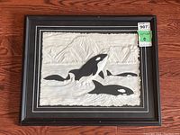 Framed paper sculpture artwork showing the entire framed piece of orca whales swimming in textured water with mountainous background.