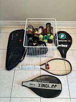 Photo of tennis racquets, carrying cases, and wire basket with tennis balls.