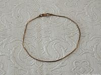 Full length view of the vintage 10K gold ladies bracelet laid flat on textured white fabric background showing chain style and shape.