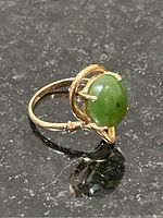 Close-up angled photo of the green jade cabochon stone in a 14K gold ring on a black surface.