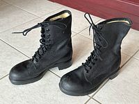 Angled view of pair of black textured leather military combat boots with laces tied, showing outer sides and front angle.