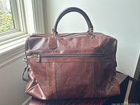 Front view of cognac colored leather duffle bag with outer zippered pocket and handles