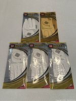 Five Wilson Dry Fit left hand ladies golf gloves in original packaging; 4 white medium size and 1 tan large size.