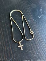 Full view of the 14k gold cross pendant hanging on the gold-tone chain, laid on a dark surface.