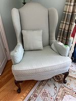 Front view of upholstered wingback armchair with removable square pillow
