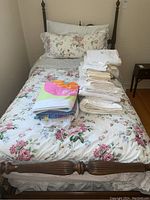 Bed with floral fitted sheet and pillowcases plus folded towels and pillows displayed on top