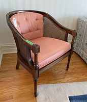 Front side angle of the wooden arm chair with cane sides and pink cushions on hardwood floor.