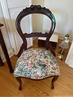 Full front view of wooden hoop back chair with floral upholstered seat showing carved floral decoration at the top of the backrest and cabriole legs.