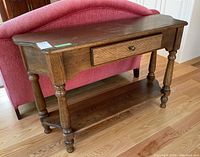 Front angled view of the wood console table showing the turned legs, single drawer with knob, and lower shelf.