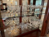 Two shelves of crystal glassware including wine glasses, flutes, snifters, and aperitif glasses arranged inside a mirrored back cabinet.