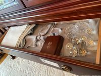 Photo of an open wooden drawer showing crystal cutter rests, coasters, wooden box with playing cards, and paperweight.
