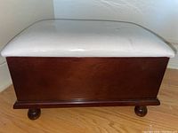 Front view of the wooden foot rest with white upholstered cushioned top.