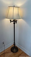 Full view of entire floor lamp standing lit in corner, showing metal base and fabric shade.