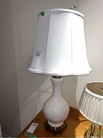 Full view of the white porcelain lamp with metal base and white fabric lampshade, placed on wooden surface next to smaller lamp.