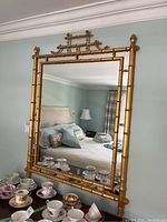 Front view of rectangular mirror with gilded bamboo-style frame hung on wall above dresser.