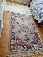 Large pink floral patterned rug on hardwood floor next to bed with floral bedspread