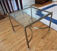 Square side table with clear beveled glass top and brass frame placed on wood floor, showing vertical ribbing on legs and rounded feet.