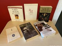 Front view of six adult sexual research and reference books on wood table with red wall background.