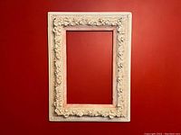 Front view of large rectangular antique white gesso frame with detailed floral motifs.