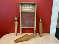 Front view of antique wooden wash board with glass scrubbing surface and three wooden pestle grinders in front.