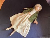 Full view of the vintage Art Deco French doll lying flat, showing long limbs, cream dress, green velvet jacket, and fabric construction.