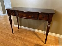 Front angled view of the dark wood hallway table showing the three drawers and turned legs, with visible scratch on top surface.
